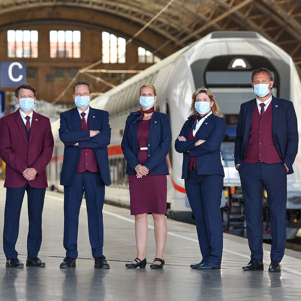 Mehrere Bahnmitarbeiter stehen mit Masken in einem Bahnhof