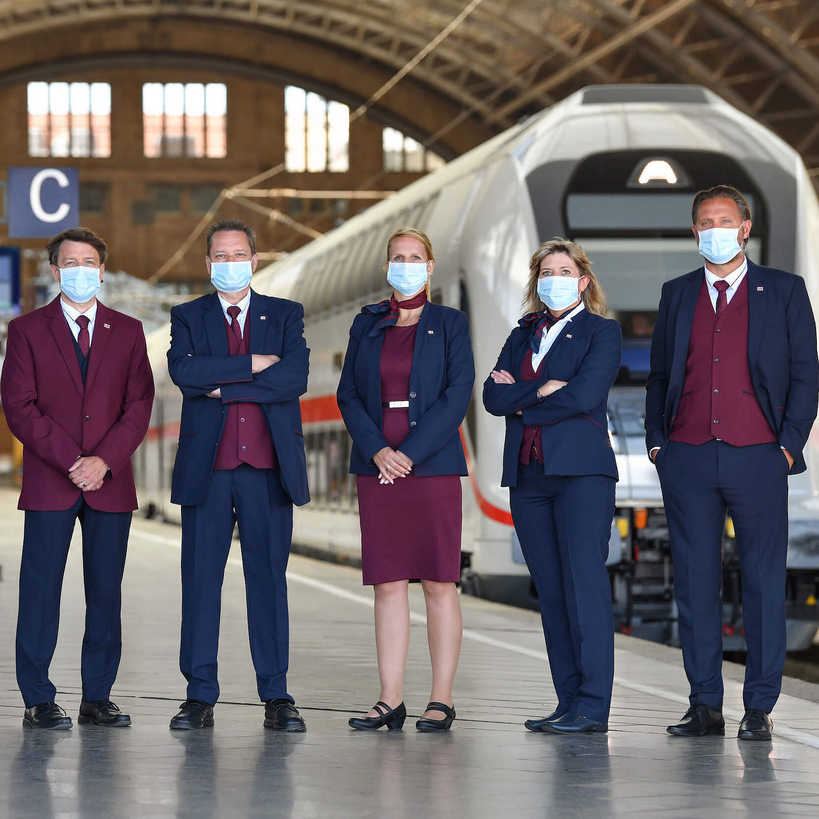 Mehrere Bahnmitarbeiter stehen mit Masken in einem Bahnhof