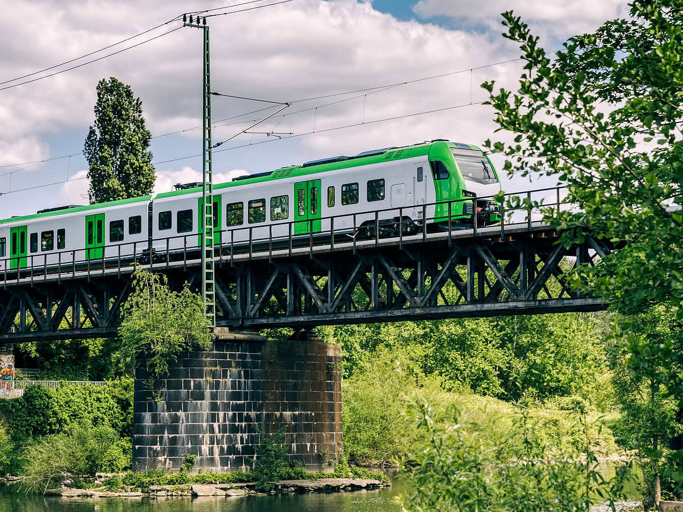 Ein Zug fährt bei Sonnenschein im Grünen über eine Brücke