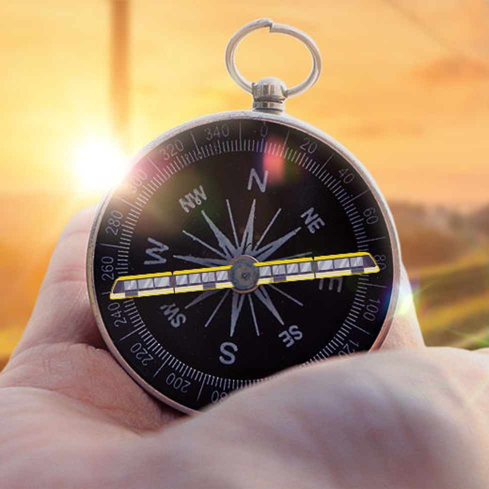 Eine Hand hält einen Kompass auf dem ein Zug abgebildet ist. Im Hintergrund sind Bahnschienen bei Sonnenuntergang zu sehen.