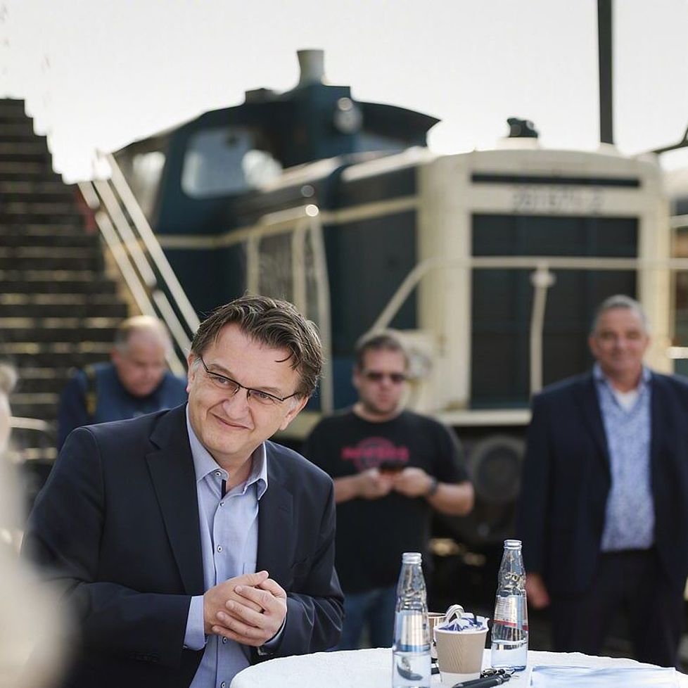 Das Foto zeigt Menschen auf einem alten Bahngelände. Im Vordergrund an einem Stehtisch in einer Gesprächssituation.