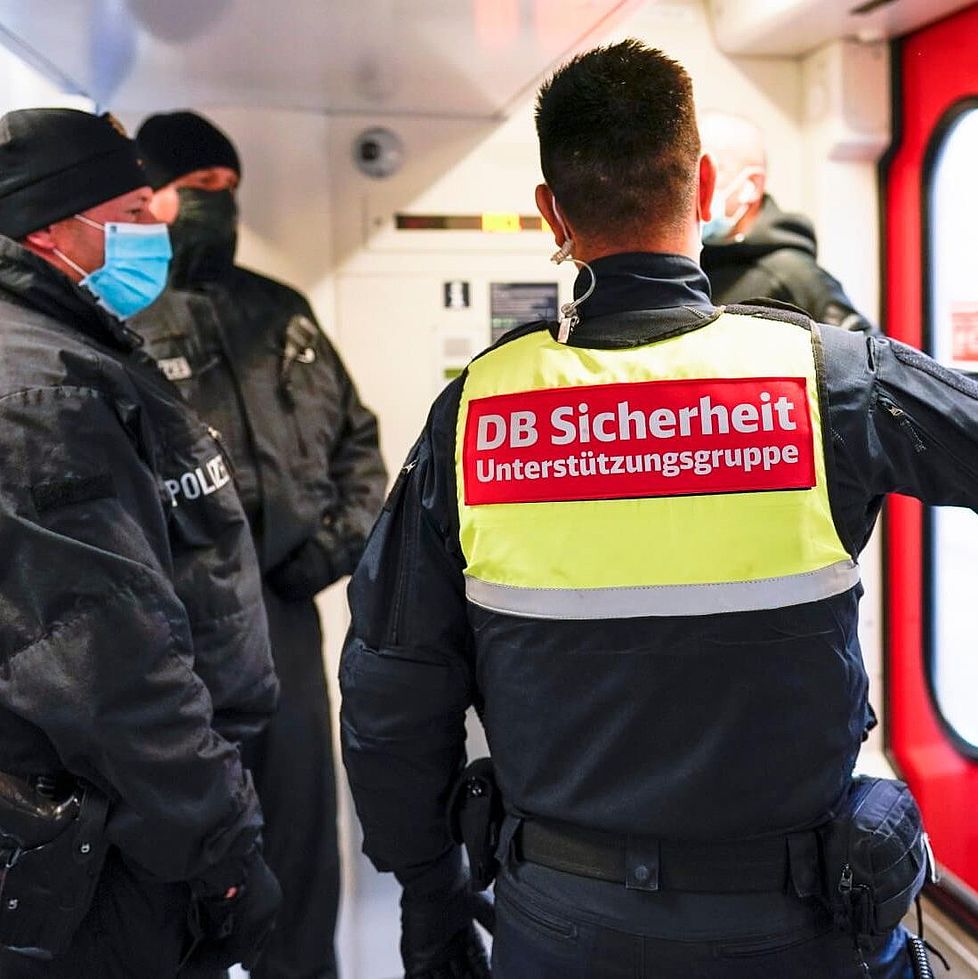 Ein Mitarbeiter der DB Sicherheit und mehrere Polizisten stehen eim EIngangsbereich eines Zuges.