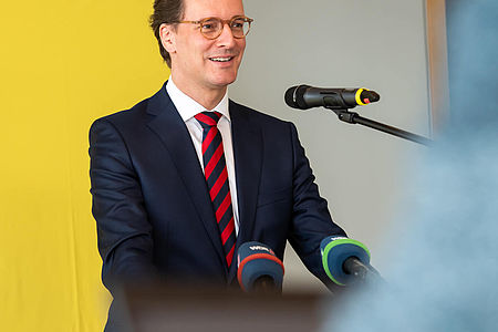 NRW-Verkehrsminister Hendrik Wüst steht an einem Podium und hält eine Rede.