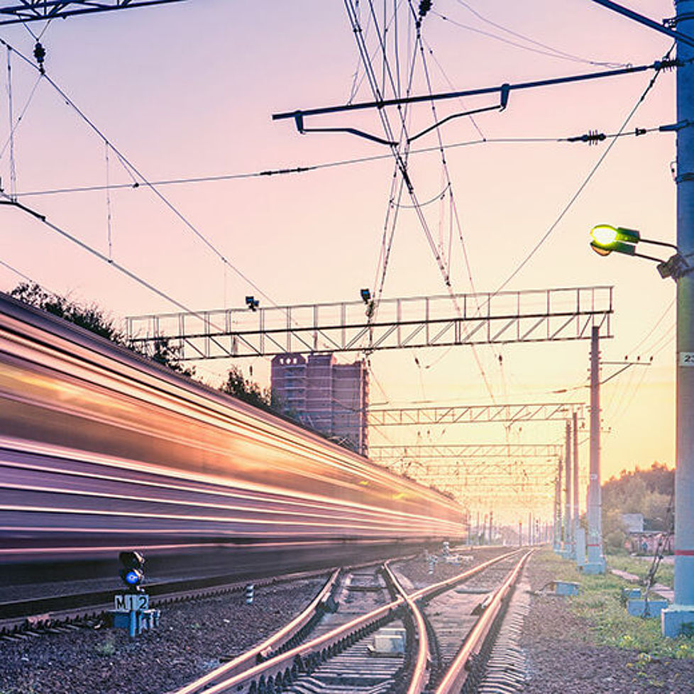 Ein Zug fährt bei Sonnenaufgang schnell ein Gleis entlang.
