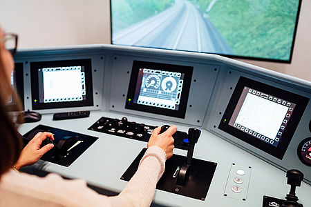 Eine Frau sitzt vor einem Fahrsimulator und steuert einen virtuellen Zug. 