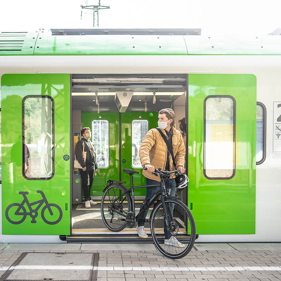 Ein junger Mann steigt mit einem Fahrrad aus einem grünen Zug aus.