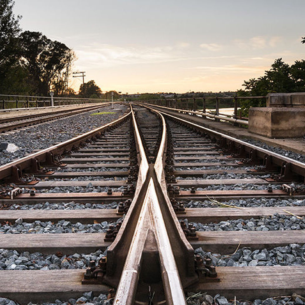 Zwei Schienen verlaufen in einem Gleisbett parallel nebeneinander bei Sonnenaufgang.