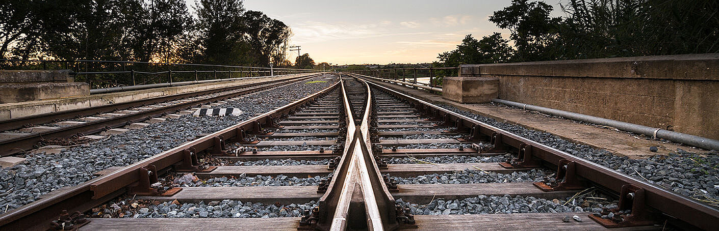 Zwei Schienen verlaufen in einem Gleisbett parallel nebeneinander bei Sonnenaufgang.