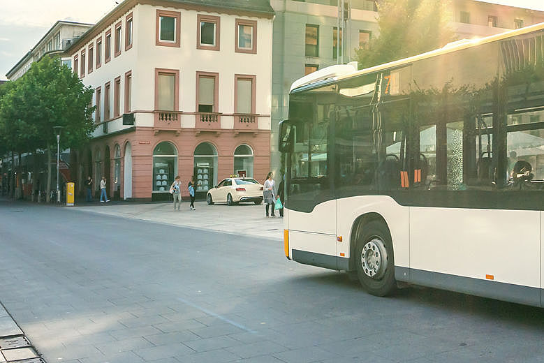 Ein schwarz-weißer Bus fährt bei sonnigem Wetter über eine breite Straße