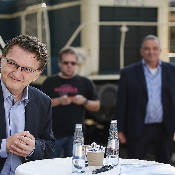 Das Foto zeigt Menschen auf einem alten Bahngelände. Im Vordergrund an einem Stehtisch in einer Gesprächssituation.